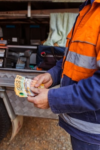 Man holding Australian dollar bills at scrap metal yard.